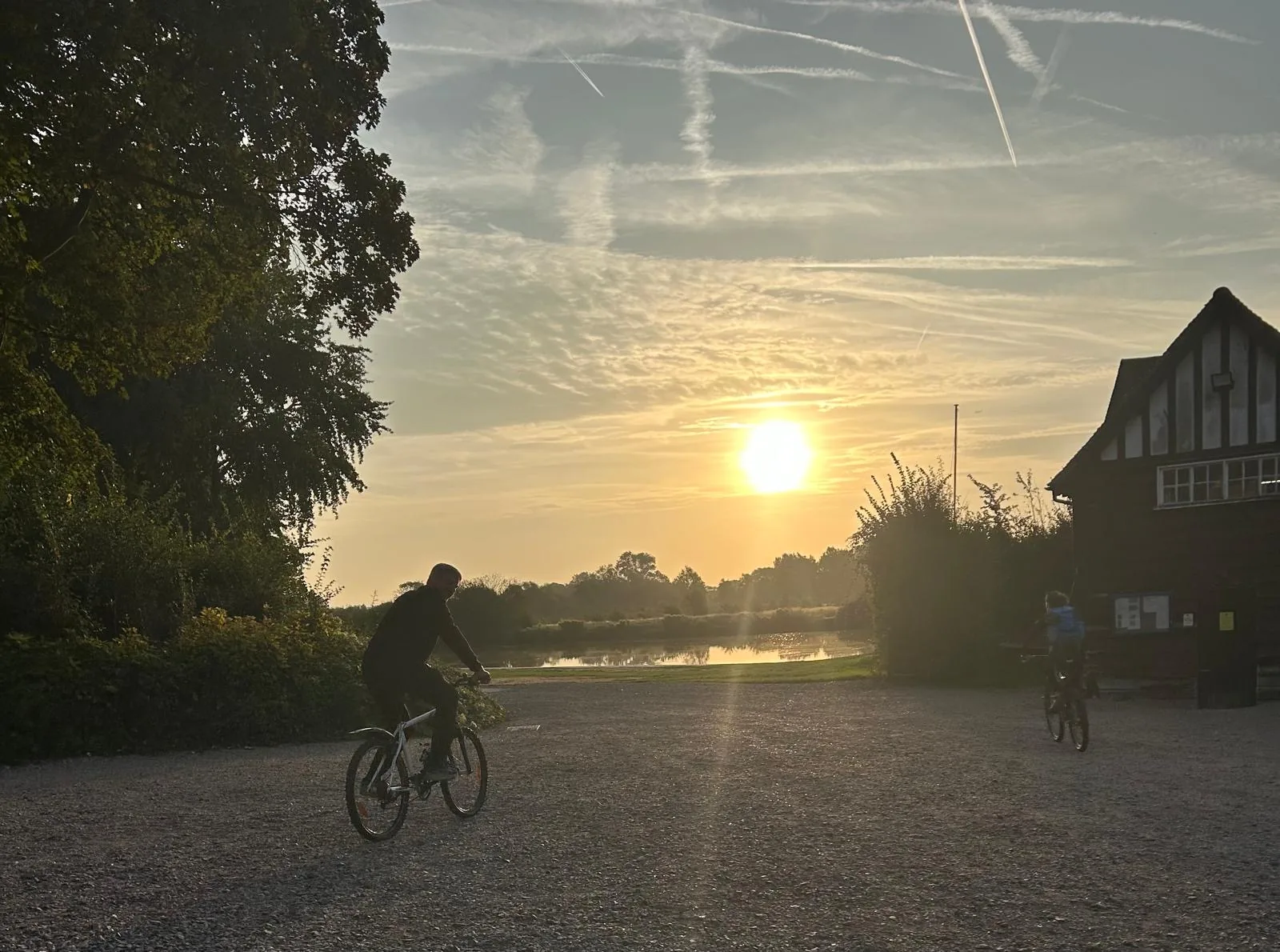 Two riders cycling past the old boathouse at sunrise beside the River Thames during the Shiplake Vikings memorial triathlon
